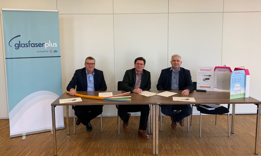 Drei Personen sitzen an einem Tisch und unterzeichnen eine gemeinsame Erklärung